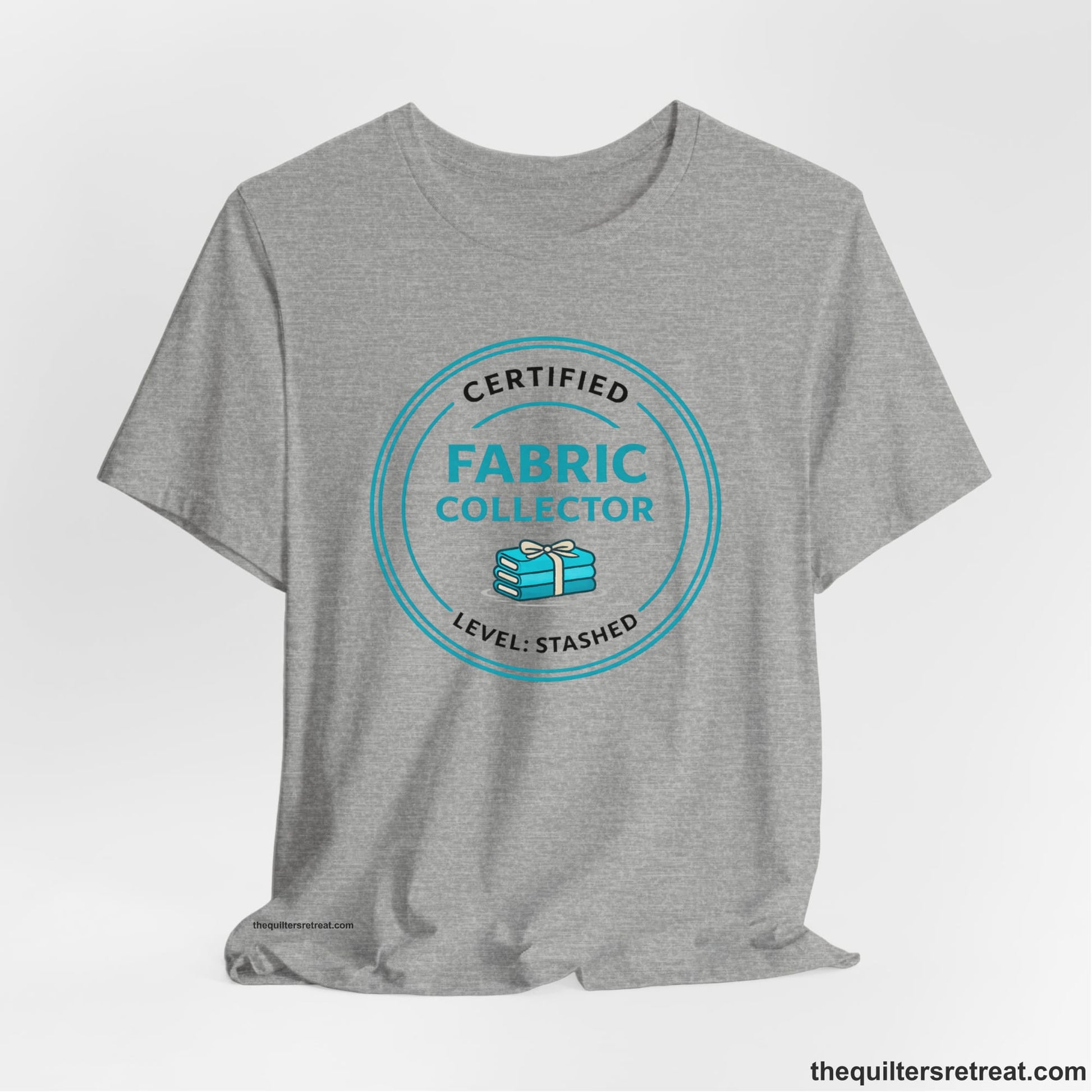A Athletic Heather Short Sleeve T-Shirt with a Circular teal logo with a whimsical fabric stack design, text "Fabric Collector".