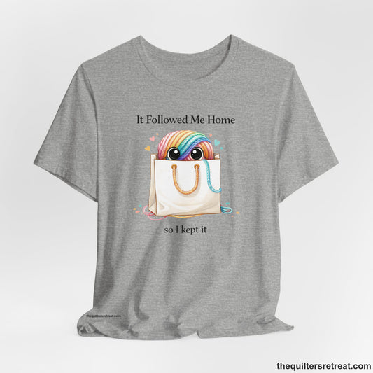 A Athletic Heather Short Sleeve T-Shirt with a Cute rainbow yarn ball with eyes in tote bag, hearts around, playful text: "It Followed Me Home so I kept it".
