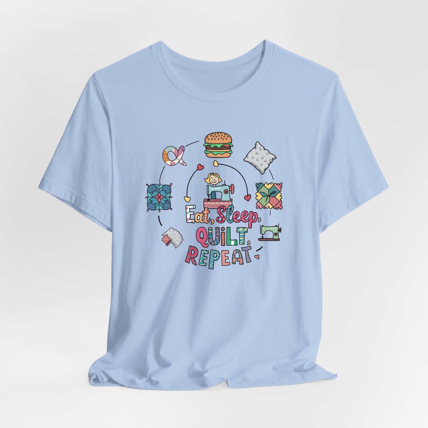 A Baby Blue Short Sleeve T-Shirt with a cute quilting elements with "Eat, Sleep, Quilt, Repeat" text in playful style
