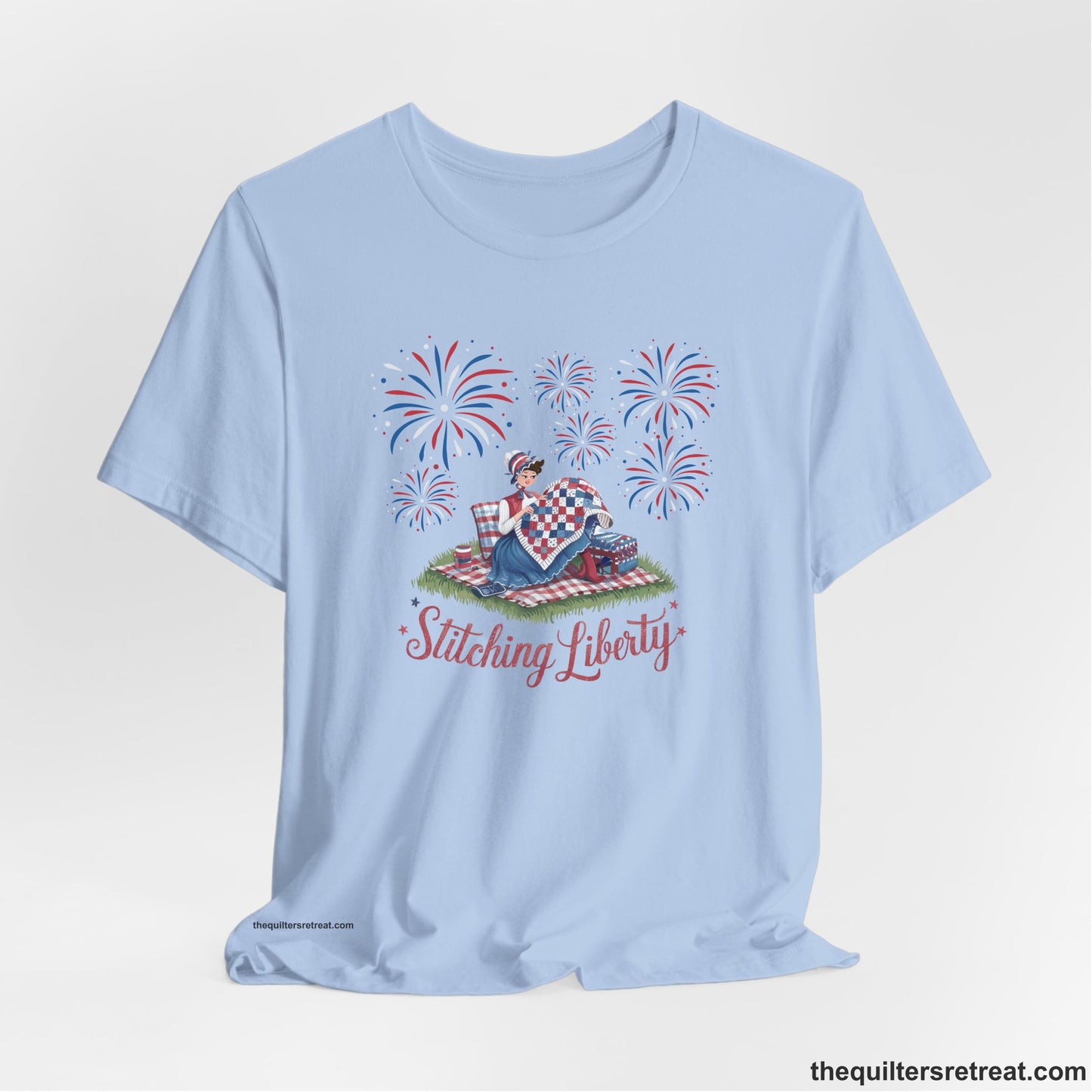 A Baby Blue Short Sleeve T-Shirt with a vintage illustration of woman quilting with fireworks and "Stitching Liberty" text in patriotic style