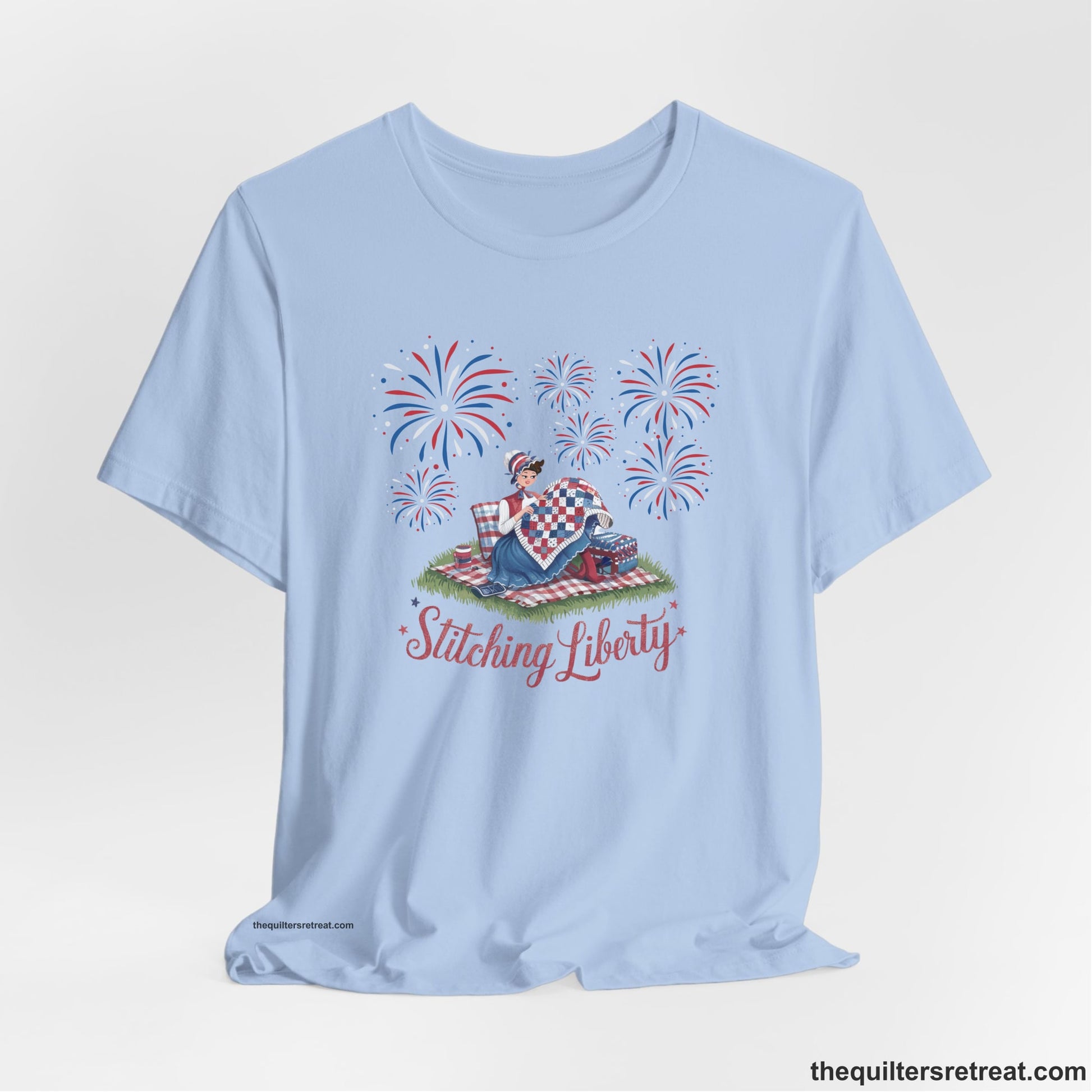 A Baby Blue Short Sleeve T-Shirt with a vintage illustration of woman quilting with fireworks and "Stitching Liberty" text in patriotic style