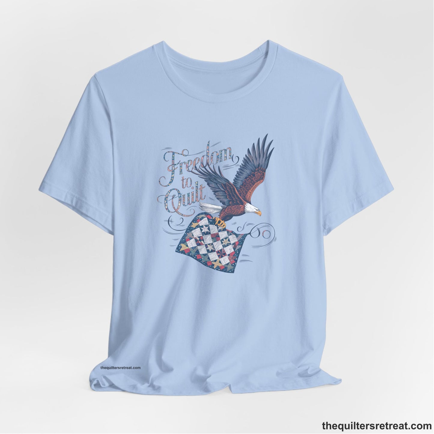 A Baby Blue Short Sleeve T-Shirt with a freedom to quilt text with an eagle carrying a colorful patchwork quilt in vintage style