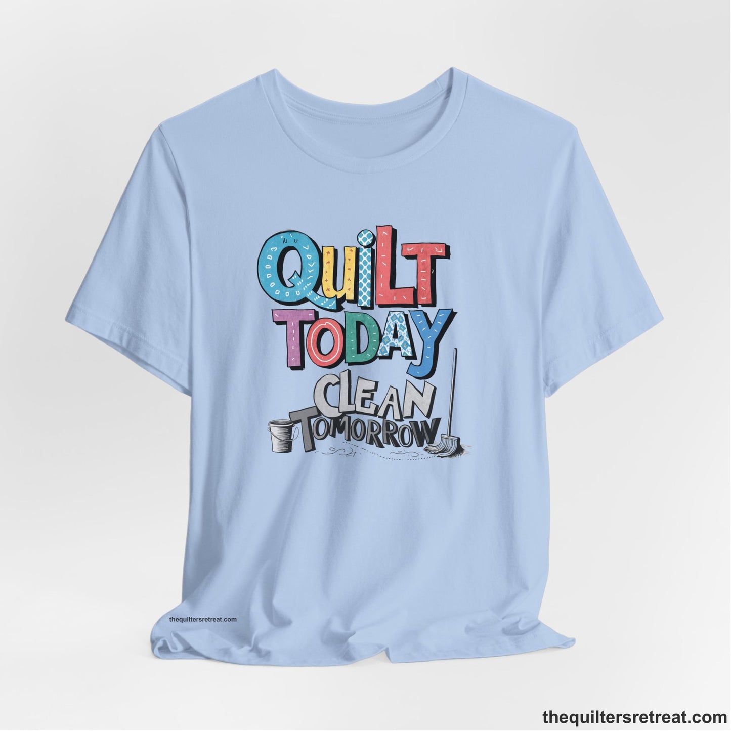 A Baby Blue Short Sleeve T-Shirt with a playful "Quilt Today Clean Tomorrow" text with colorful patterns and cleaning tools illustration
