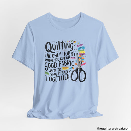 A Baby Blue Short Sleeve T-Shirt with a quilting-themed text with colorful fabric pieces and scissors in a whimsical style
