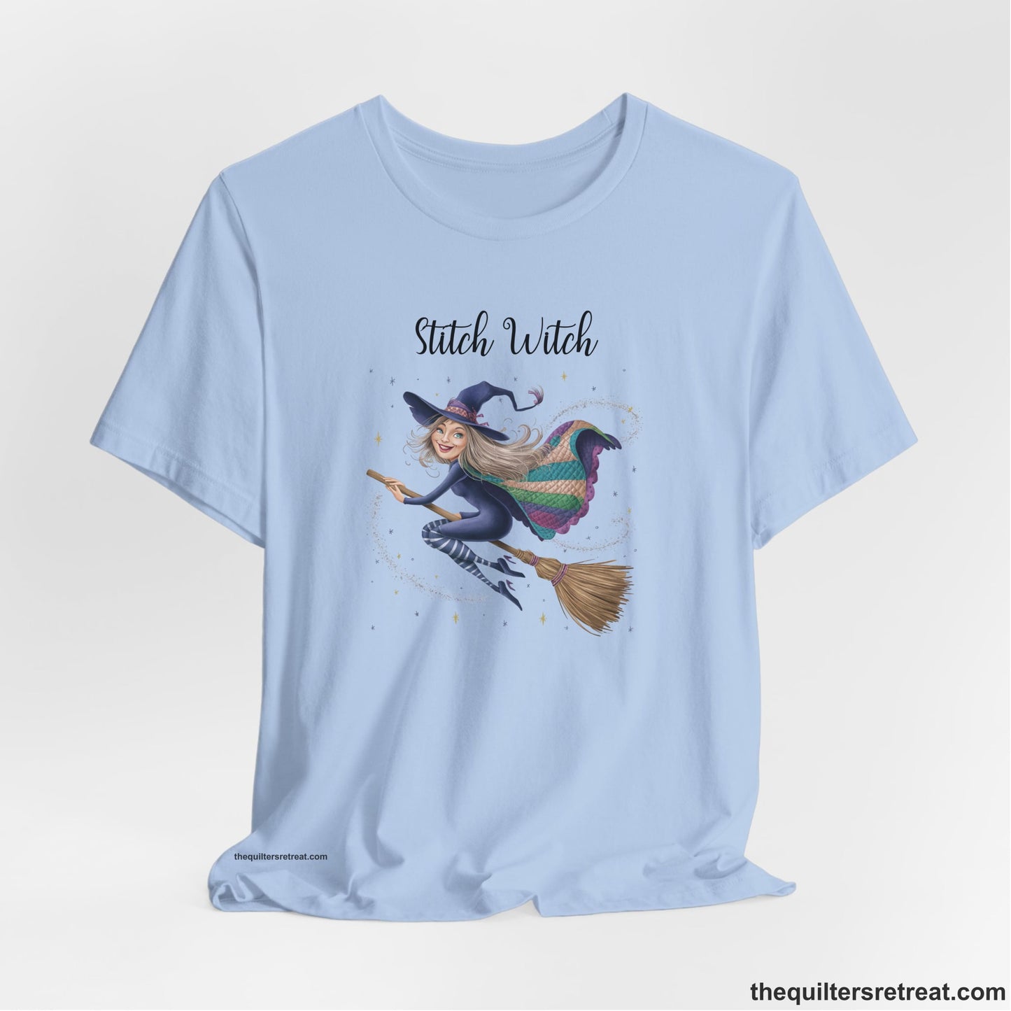 A Baby Blue Short Sleeve T-Shirt with a playful witch on broomstick with patchwork cape and starry background in a whimsical style