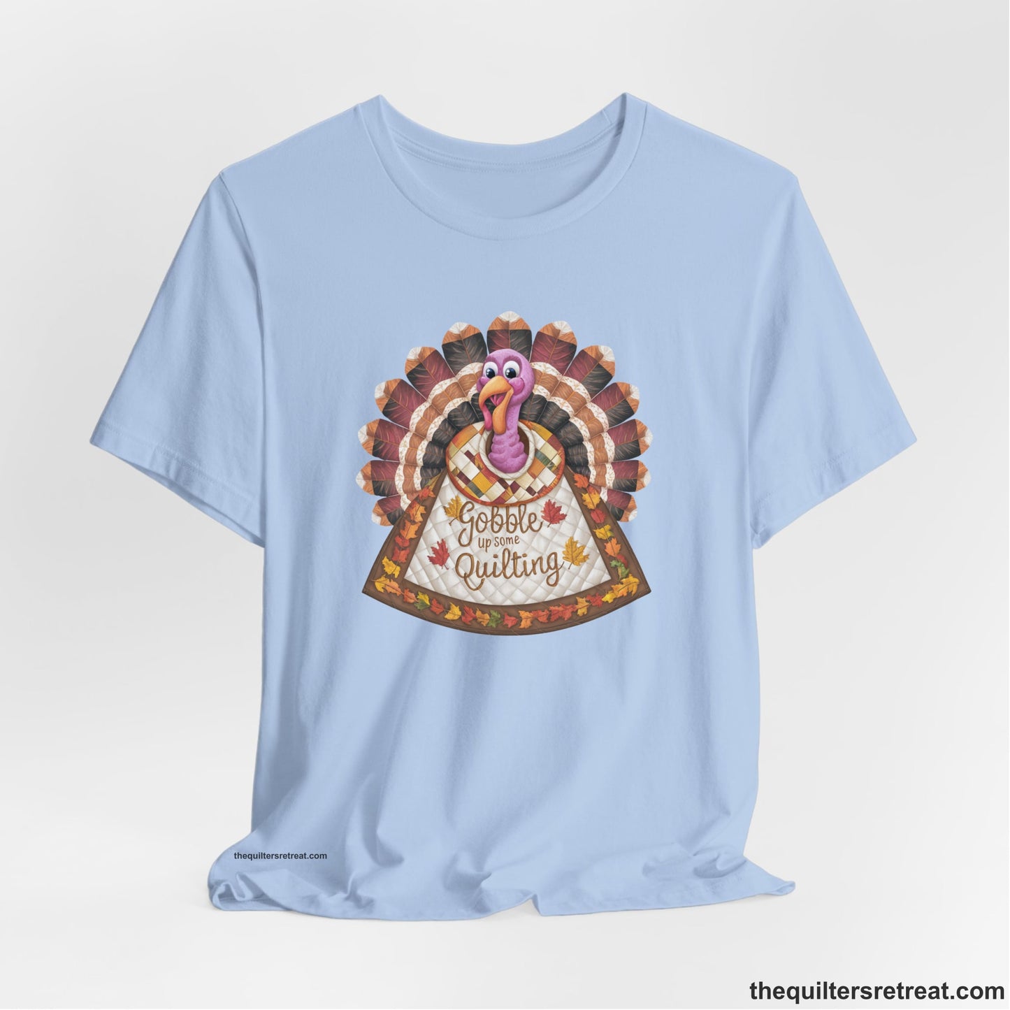 A Baby Blue Short Sleeve T-Shirt with a colorful turkey with quilted feathers and "Gobble Up Some Quilting" text in a playful style