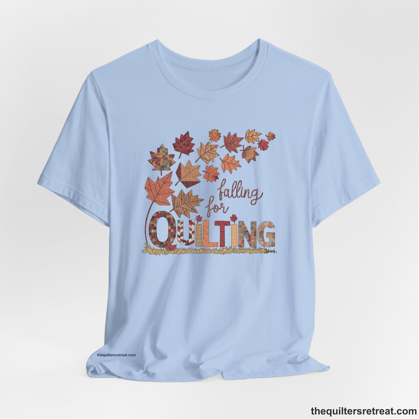 A Baby Blue Short Sleeve T-Shirt with a falling autumn leaves and "Falling for Quilting" text in a patchwork style