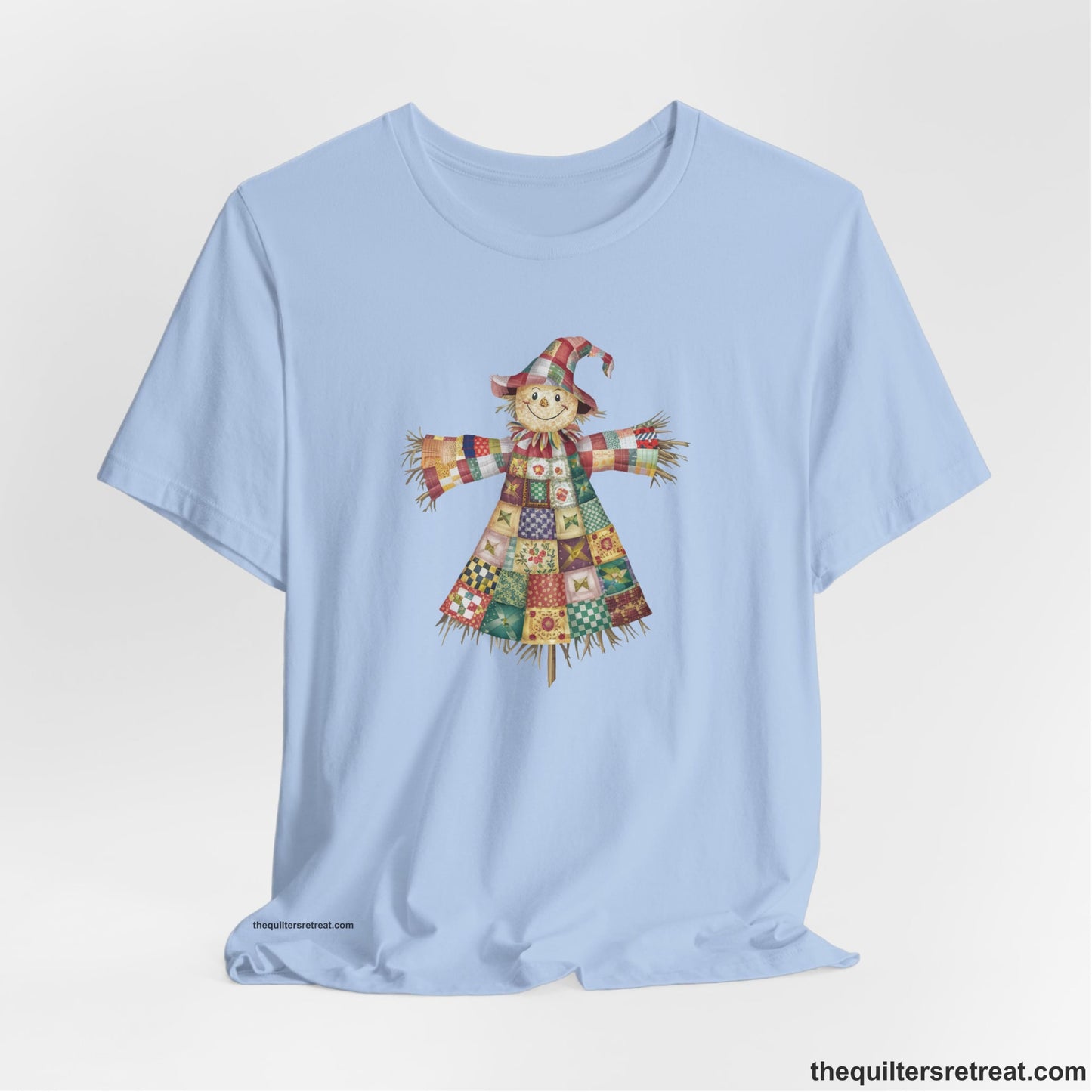 A Baby Blue Short Sleeve T-Shirt with a patchwork scarecrow with a cheerful face in a whimsical style