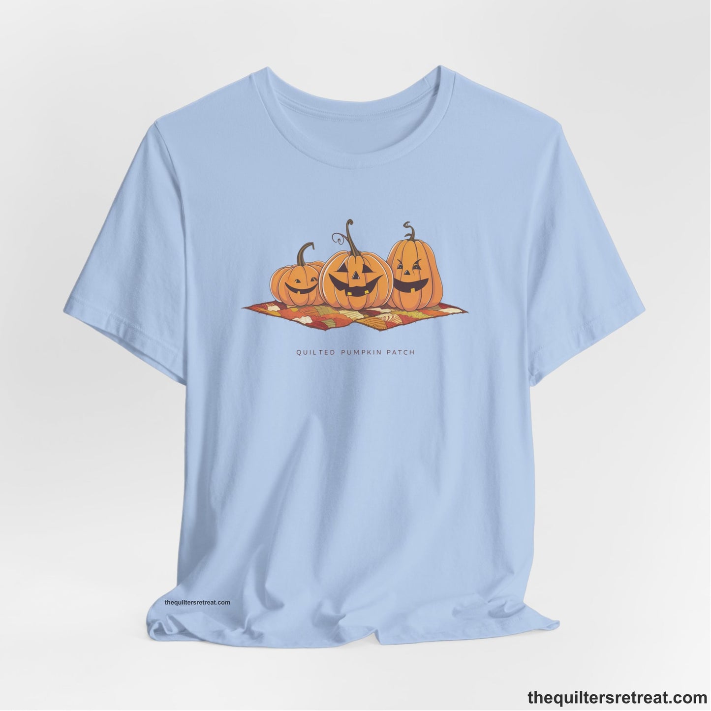 A Baby Blue Short Sleeve T-Shirt with a playful jack-o'-lantern trio on a quilt with "Quilted Pumpkin Patch" text