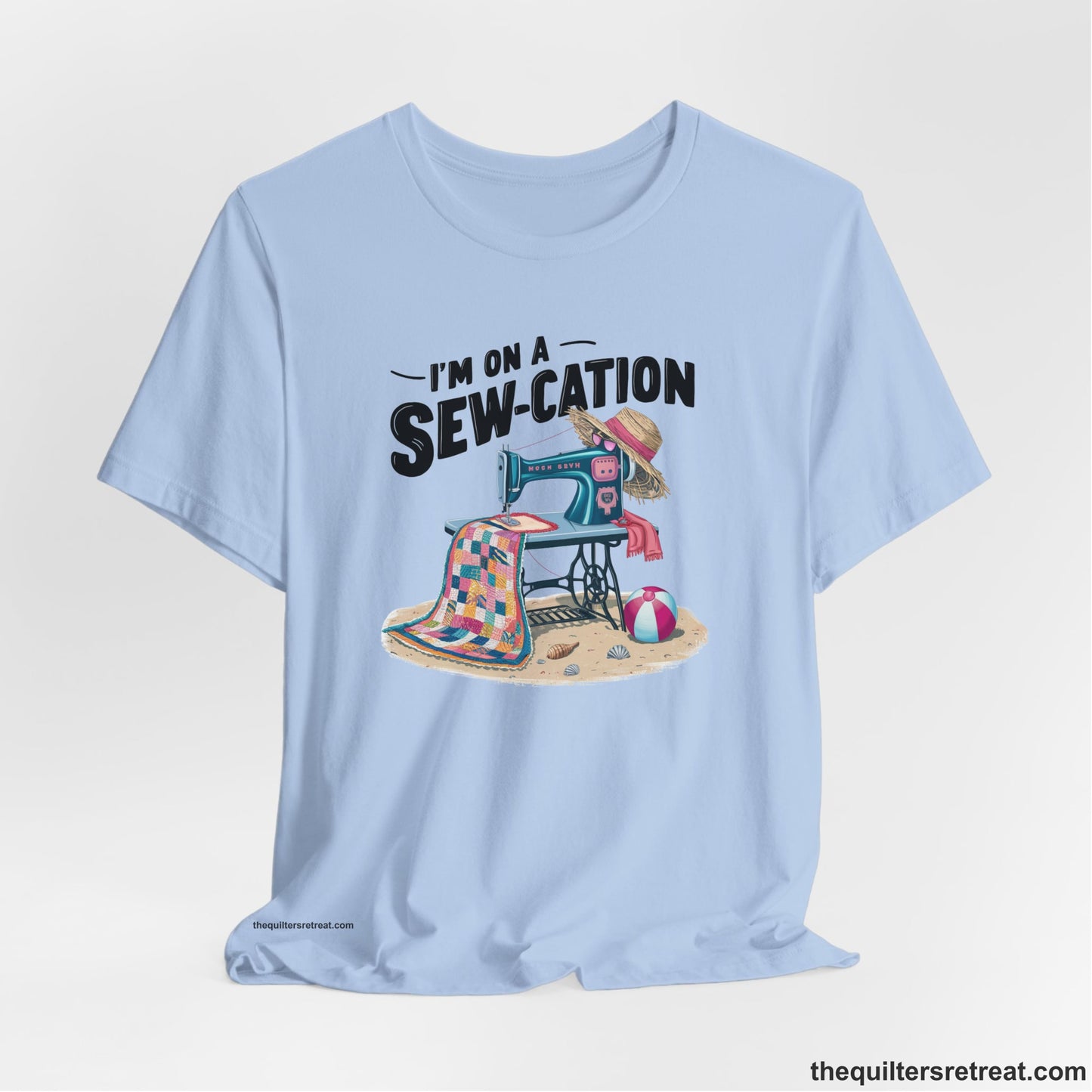 A Baby Blue Short Sleeve T-Shirt with a vintage sewing machine with colorful quilt, beach items, and "I'm On A Sew-Cation" text