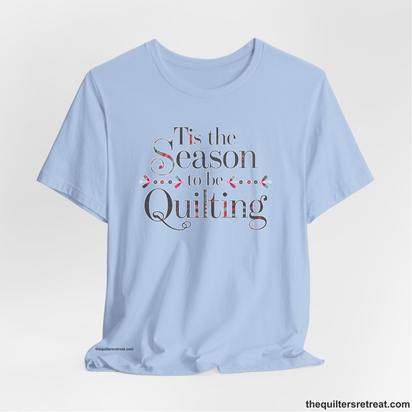 A Baby Blue Short Sleeve T-Shirt with a tis the season to be quilting text with festive patchwork pattern in a cheerful style