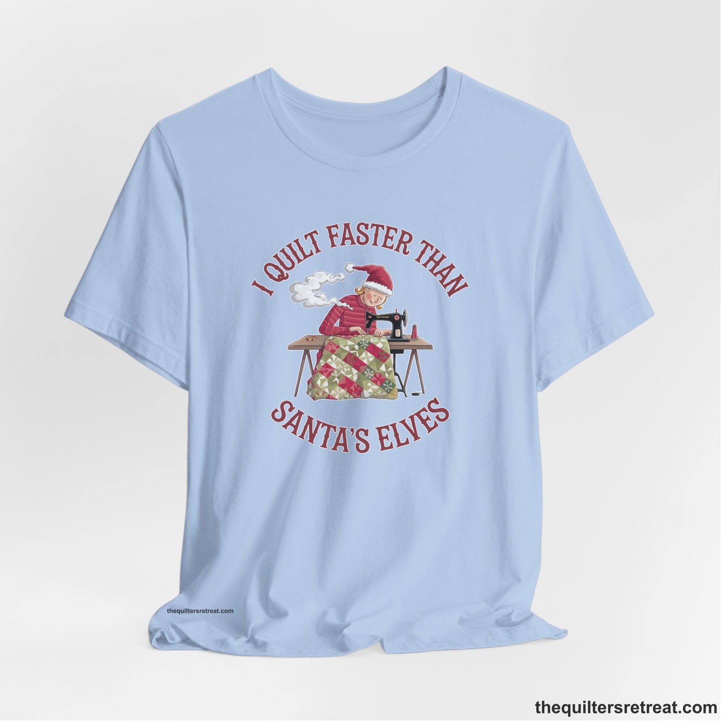A Baby Blue Short Sleeve T-Shirt with a whimsical illustration of a quilting woman with "I Quilt Faster Than Santa's Elves" text