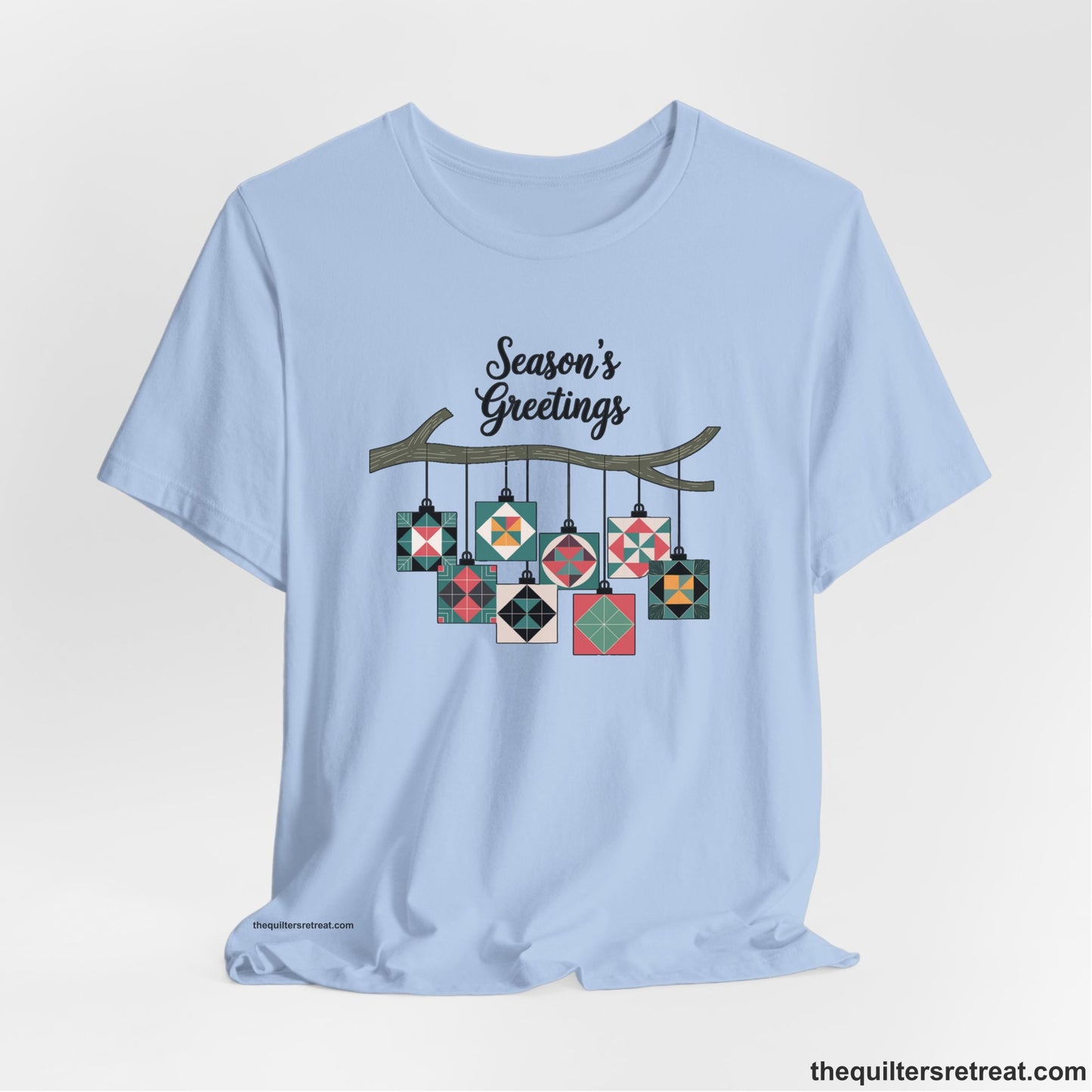 A Baby Blue Short Sleeve T-Shirt with a season's greetings text above colorful quilt block ornaments on tree branch in rustic style