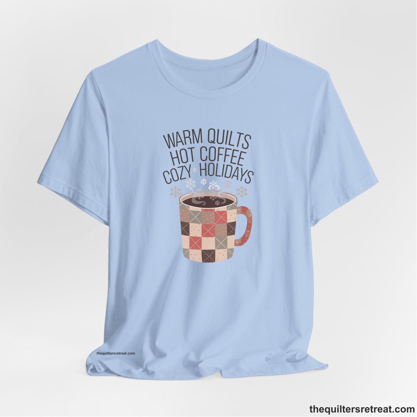 A Baby Blue Short Sleeve T-Shirt with a warm quilts hot coffee cozy holidays text with a patchwork mug and snowflakes