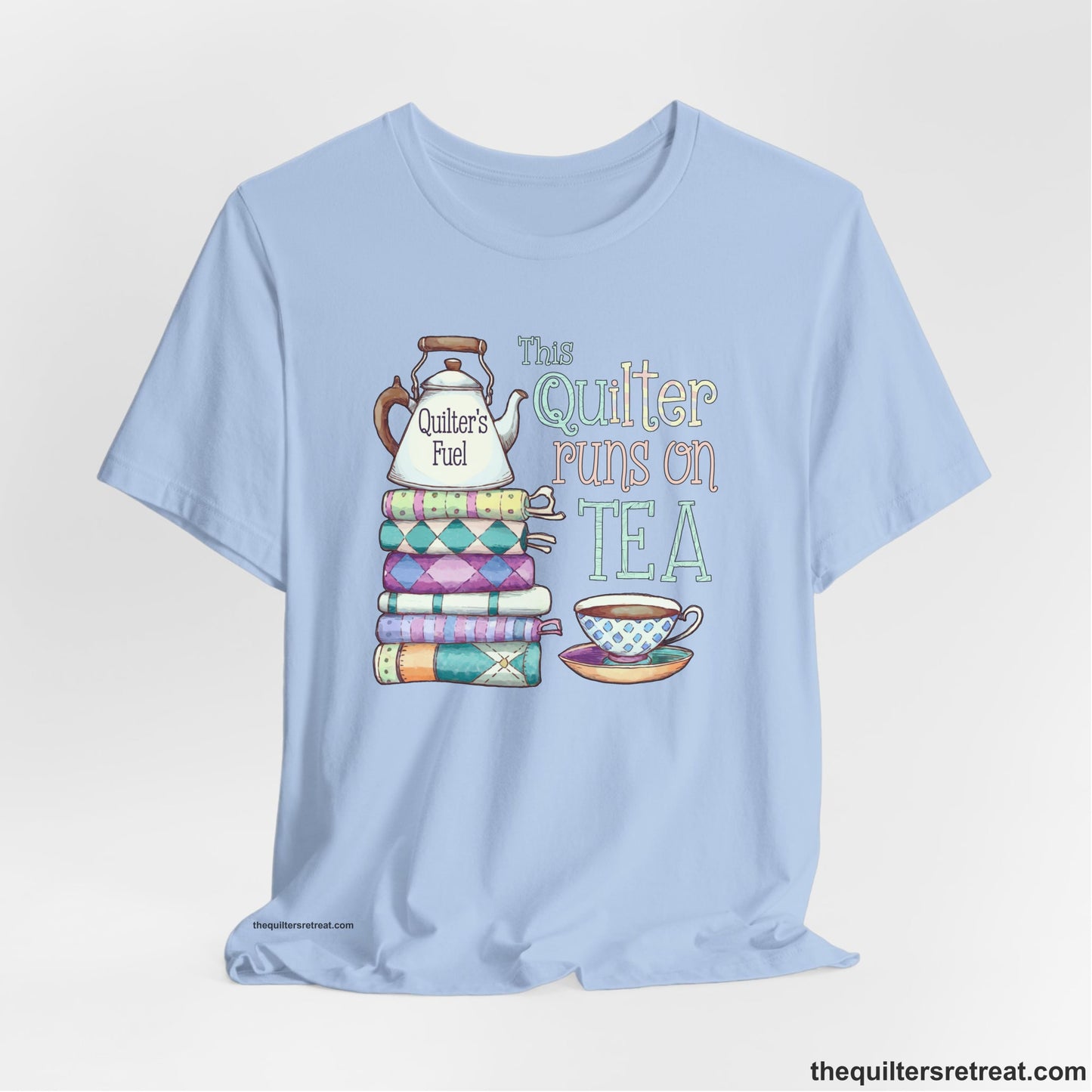 A Baby Blue Short Sleeve T-Shirt with a stack of colorful quilts with teapot and cup, whimsical "This Quilter Runs on Tea" text