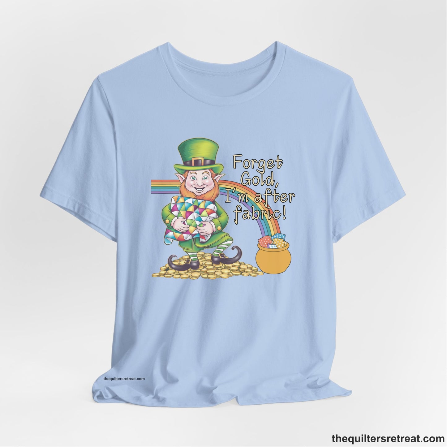 A Baby Blue Short Sleeve T-Shirt with a leprechaun with colorful quilt and rainbow, whimsical "Forget Gold, I'm after fabric!" text