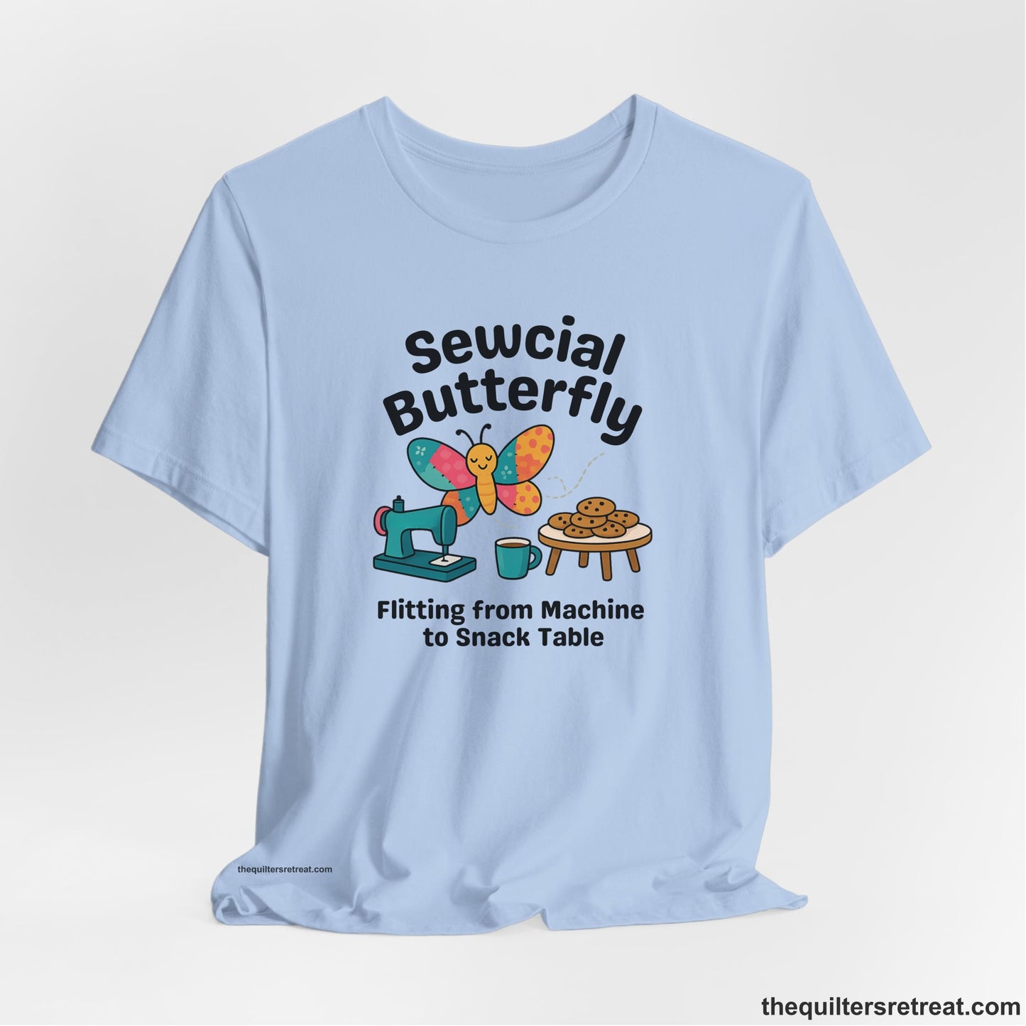 A Baby Blue Short Sleeve T-Shirt with a playful butterfly near sewing machine with cookies and coffee doodle design
