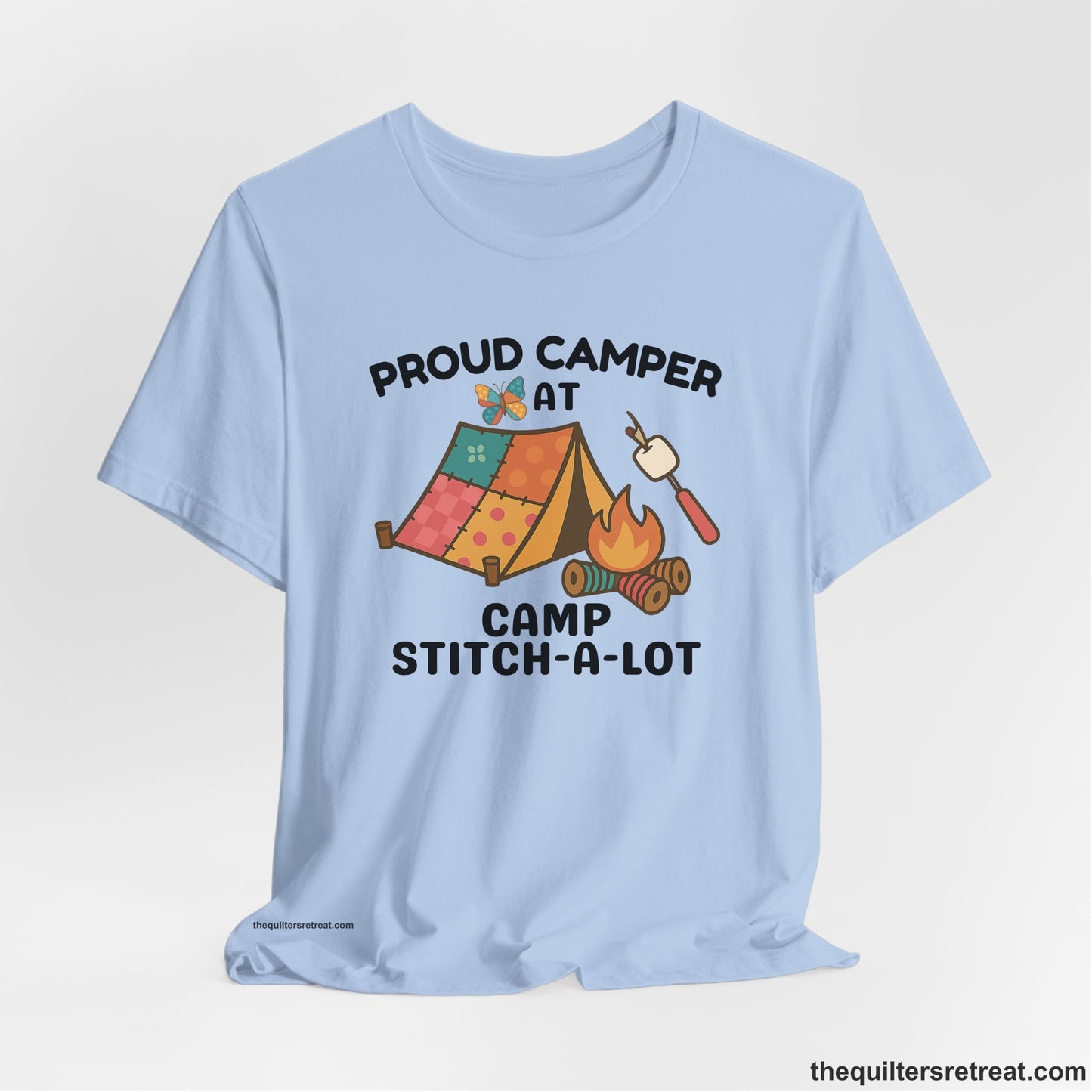 A Baby Blue Short Sleeve T-Shirt with a camping scene with patchwork tent, campfire, and whimsical butterfly and marshmallow illustration