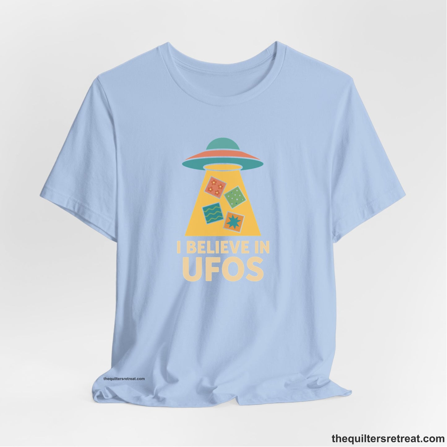 A Baby Blue Short Sleeve T-Shirt with a colorful UFO with quilt patterns and bold "I Believe in UFOs" text in retro style