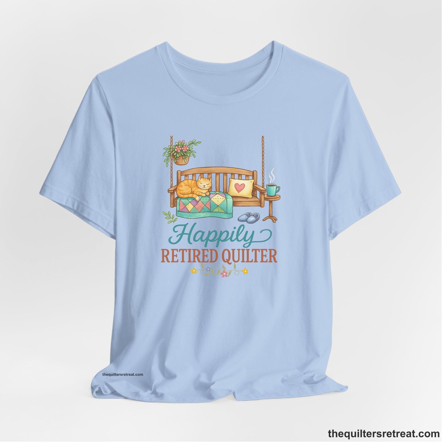 A Baby Blue Short Sleeve T-Shirt with a hanging bench with cozy cat and quilt, surrounded by plants, "Happily Retired Quilter" text