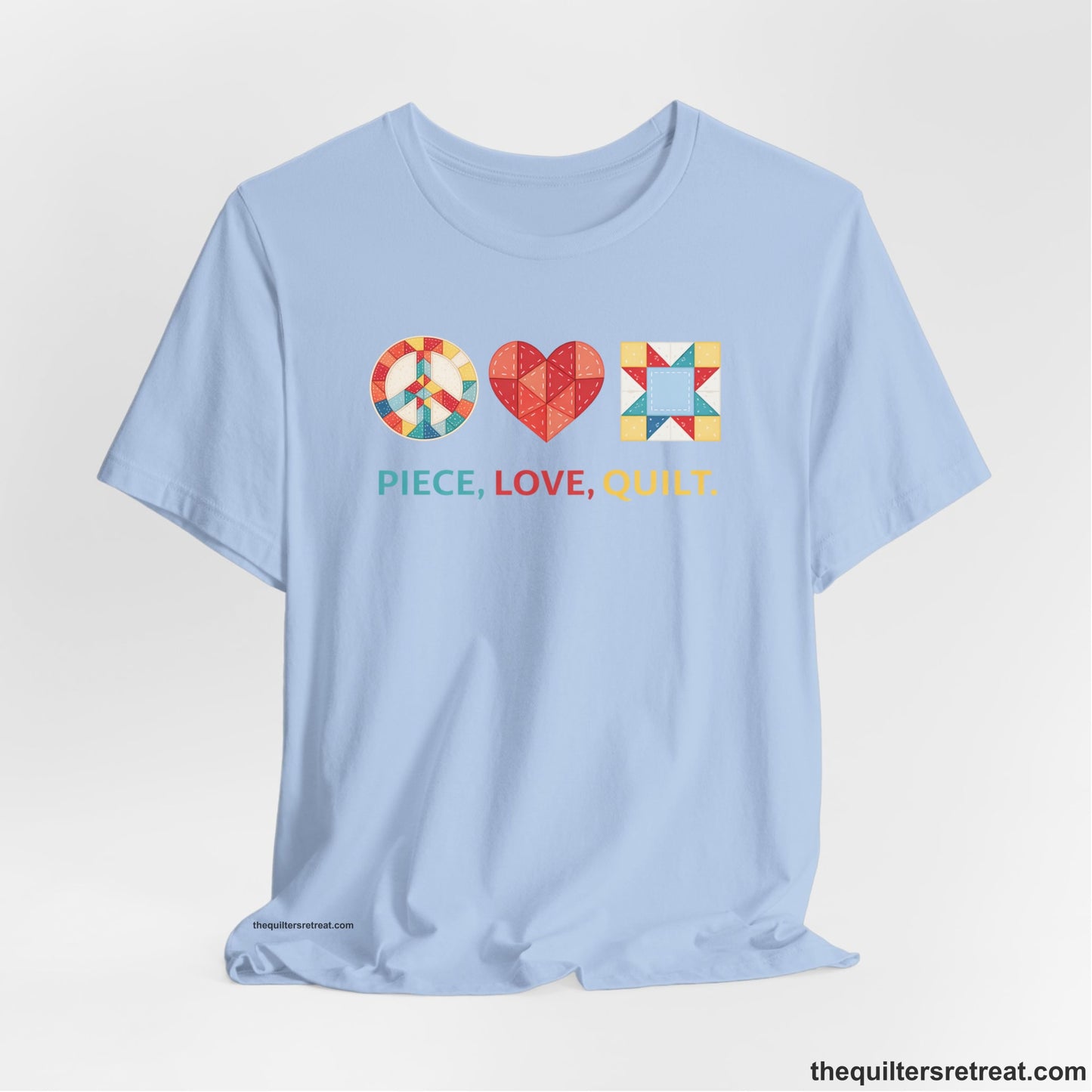 A Baby Blue Short Sleeve T-Shirt with a Colorful quilt patterns, "PIECE, LOVE, QUILT." text, whimsical style.