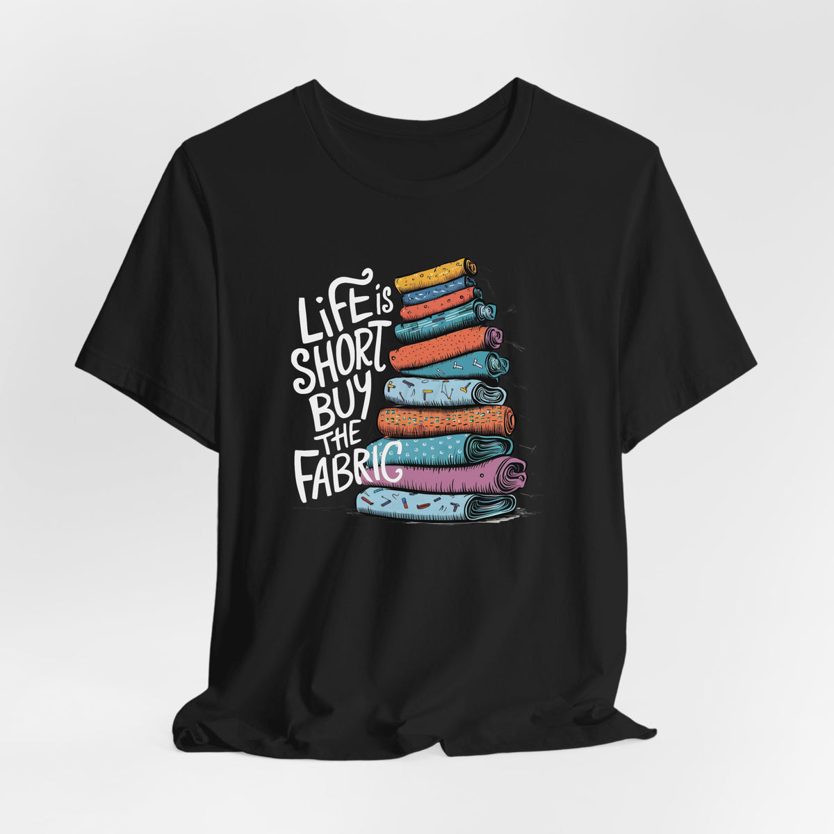 A Black Short Sleeve T-Shirt with a illustration of colorful fabric rolls with bold "Life is Short Buy the Fabric" text