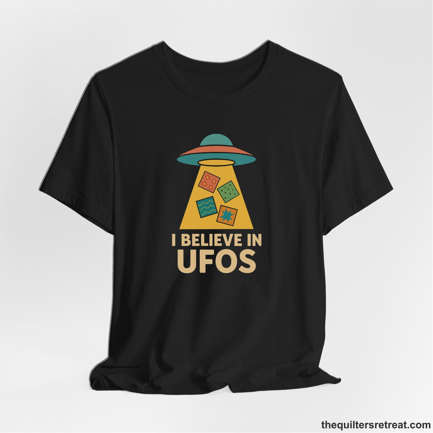 A Black Short Sleeve T-Shirt with a colorful UFO with quilt patterns and bold "I Believe in UFOs" text in retro style