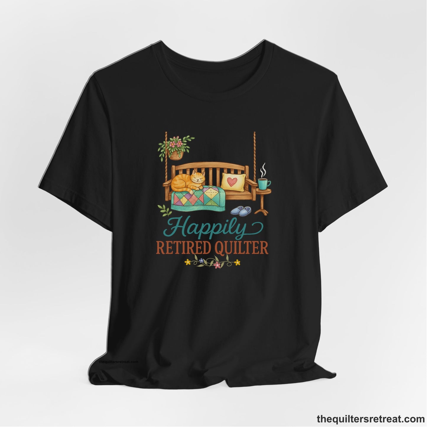 A Black Short Sleeve T-Shirt with a hanging bench with cozy cat and quilt, surrounded by plants, "Happily Retired Quilter" text