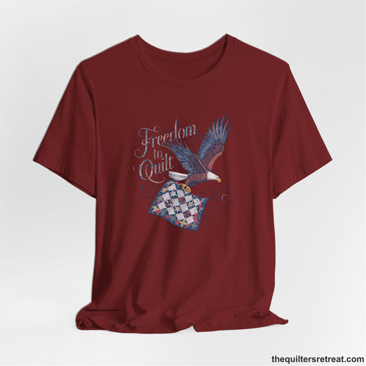 A Short Sleeve T-Shirt with a freedom to quilt text with an eagle carrying a colorful patchwork quilt in vintage style