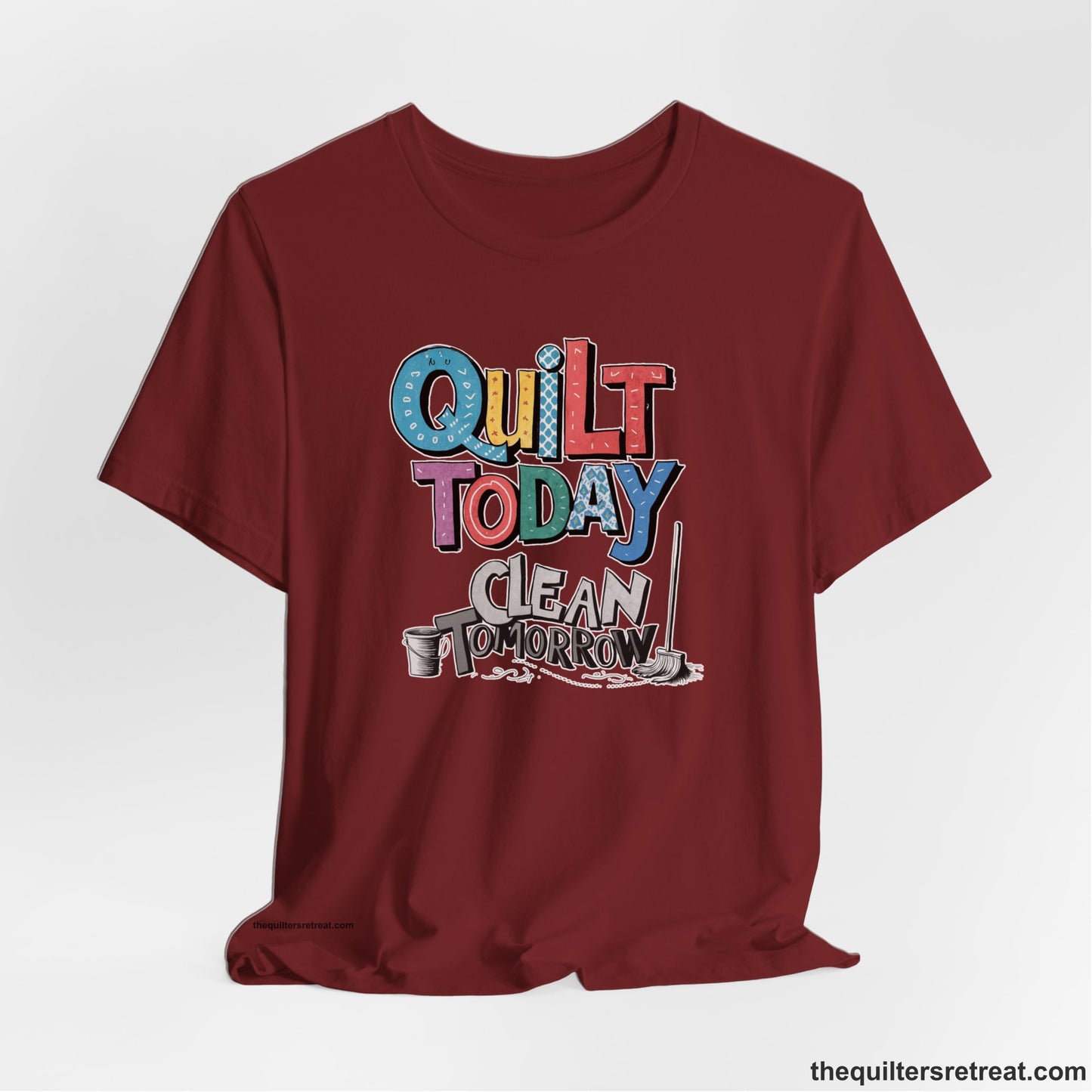 A Cardinal Short Sleeve T-Shirt with a playful "Quilt Today Clean Tomorrow" text with colorful patterns and cleaning tools illustration