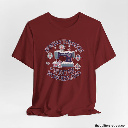 A Cardinal Short Sleeve T-Shirt with a sewing machine covered in snow with festive quilting elements and "Sewing Through a Winter Wonderland" text