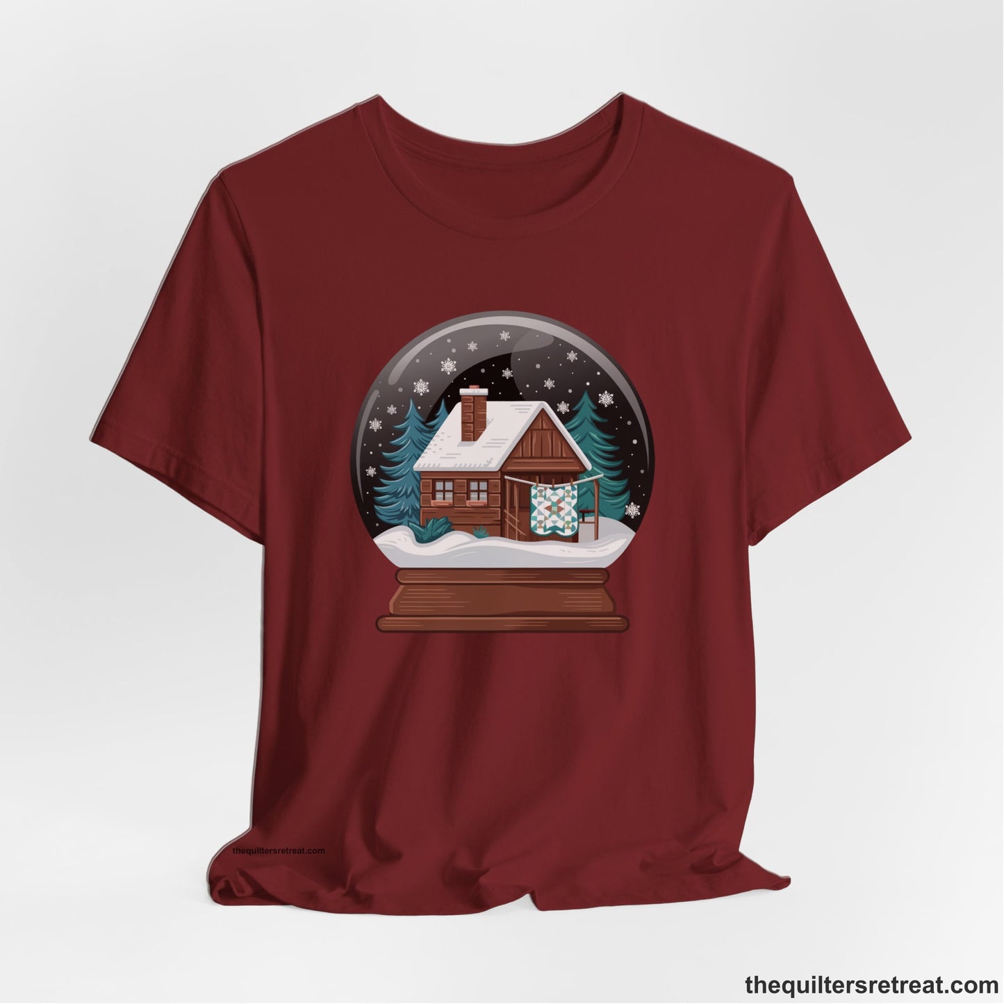 A Cardinal Short Sleeve T-Shirt with a cabin in a snow globe with snowflakes and trees, in a cozy rustic style