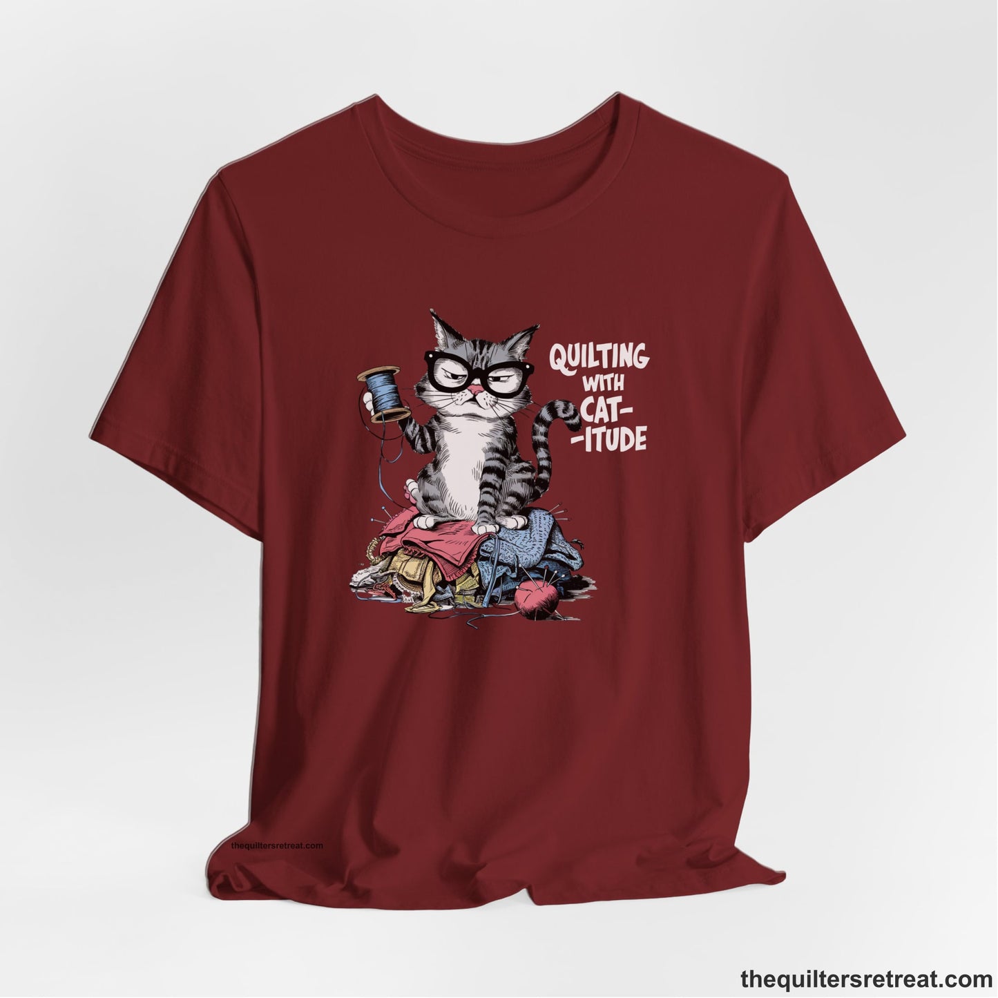 A Cardinal Short Sleeve T-Shirt with a grumpy cat holding thread spool atop fabric pile with "Quilting with Cat-itude" text