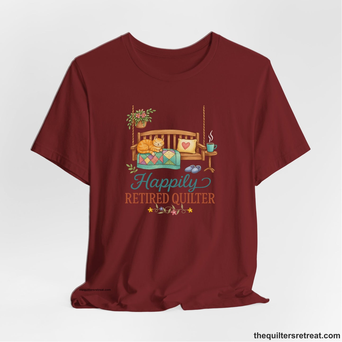 A Cardinal Short Sleeve T-Shirt with a hanging bench with cozy cat and quilt, surrounded by plants, "Happily Retired Quilter" text