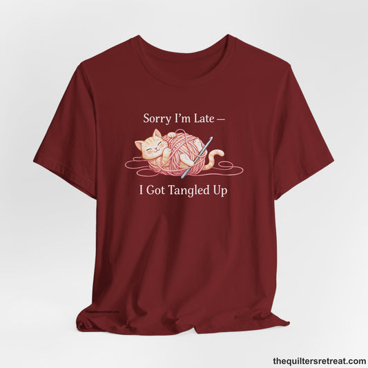 Crochet Gift: A Cardinal Short Sleeve T-Shirt with Cute cat tangled in pink yarn, whimsical style, text: "Sorry I'm Late — I Got Tangled Up"