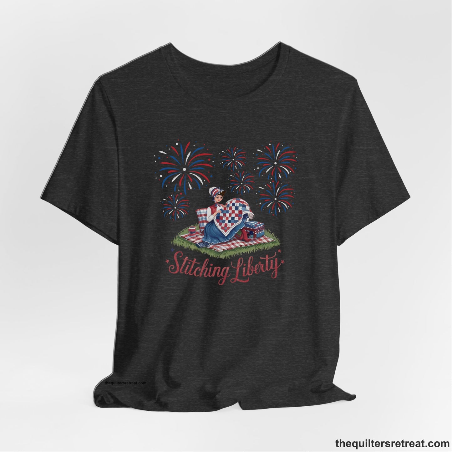 A Dark Grey Heather Short Sleeve T-Shirt with a vintage illustration of woman quilting with fireworks and "Stitching Liberty" text in patriotic style