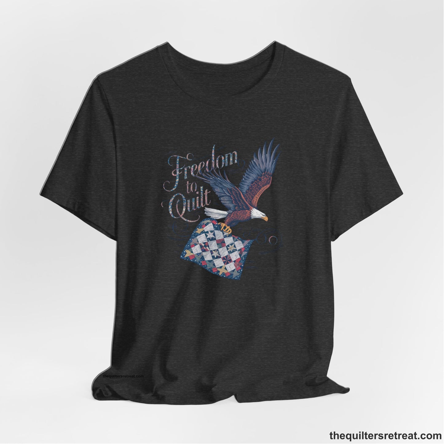 A Dark Grey Heather Short Sleeve T-Shirt with a freedom to quilt text with an eagle carrying a colorful patchwork quilt in vintage style