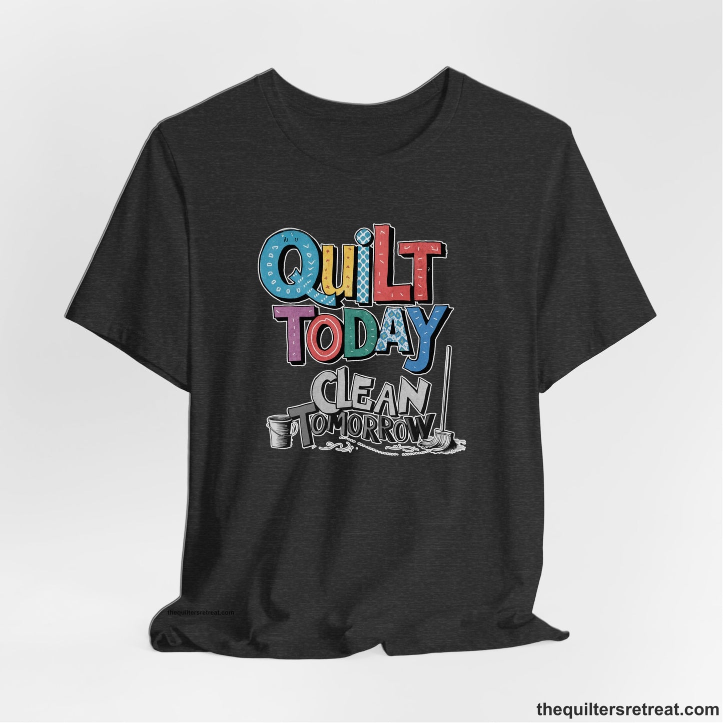 A Dark Grey Heather Short Sleeve T-Shirt with a playful "Quilt Today Clean Tomorrow" text with colorful patterns and cleaning tools illustration
