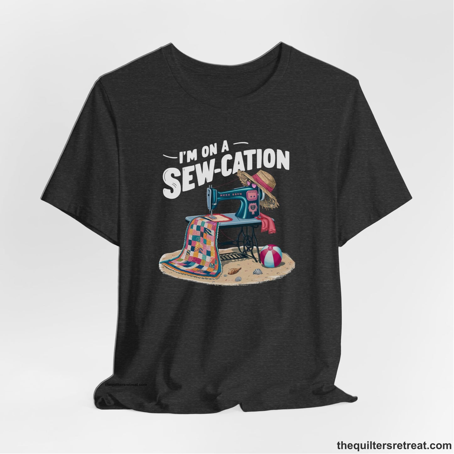 A Dark Grey Heather Short Sleeve T-Shirt with a vintage sewing machine with colorful quilt, beach items, and "I'm On A Sew-Cation" text