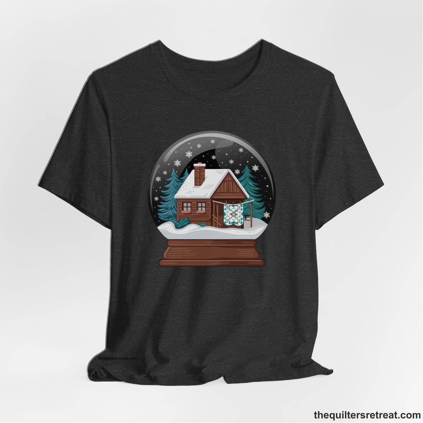 A Dark Grey Heather Short Sleeve T-Shirt with a cabin in a snow globe with snowflakes and trees, in a cozy rustic style