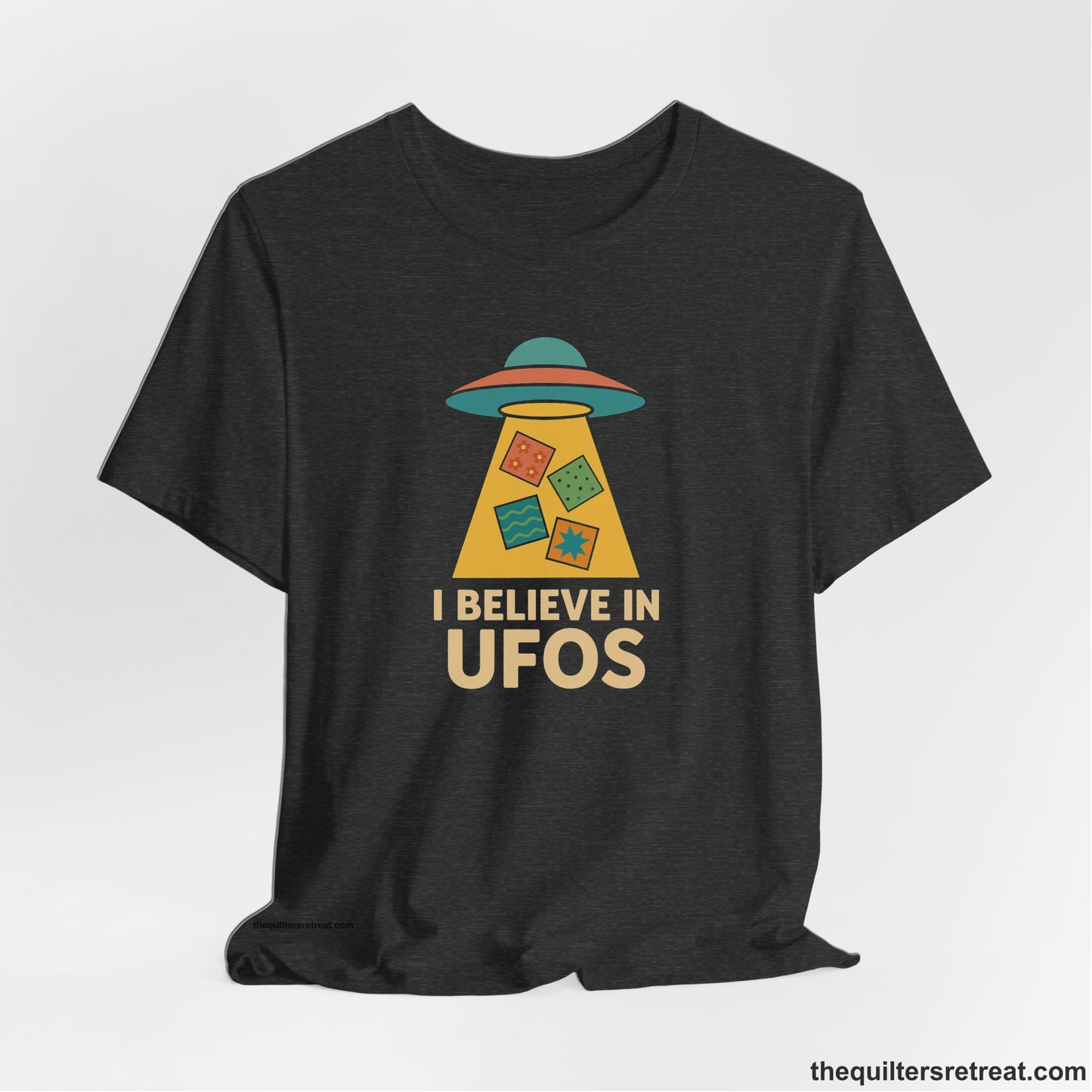 A Dark Grey Heather Short Sleeve T-Shirt with a colorful UFO with quilt patterns and bold "I Believe in UFOs" text in retro style