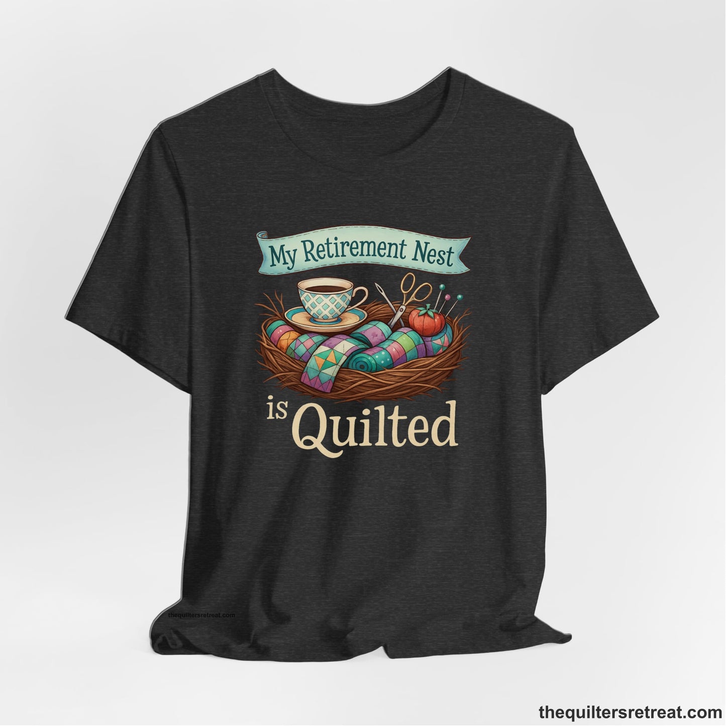 A Dark Grey Heather Short Sleeve T-Shirt with a My Retirement Nest is Quilted text with a cozy sewing elements illustration