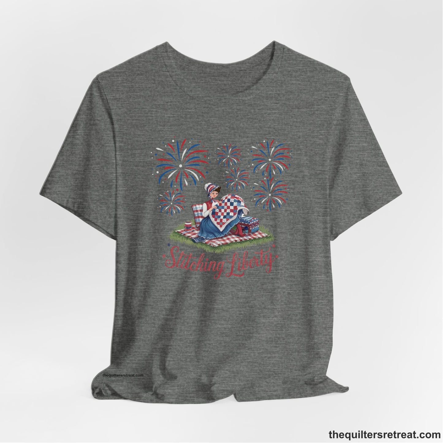 A Deep Heather Short Sleeve T-Shirt with a vintage illustration of woman quilting with fireworks and "Stitching Liberty" text in patriotic style