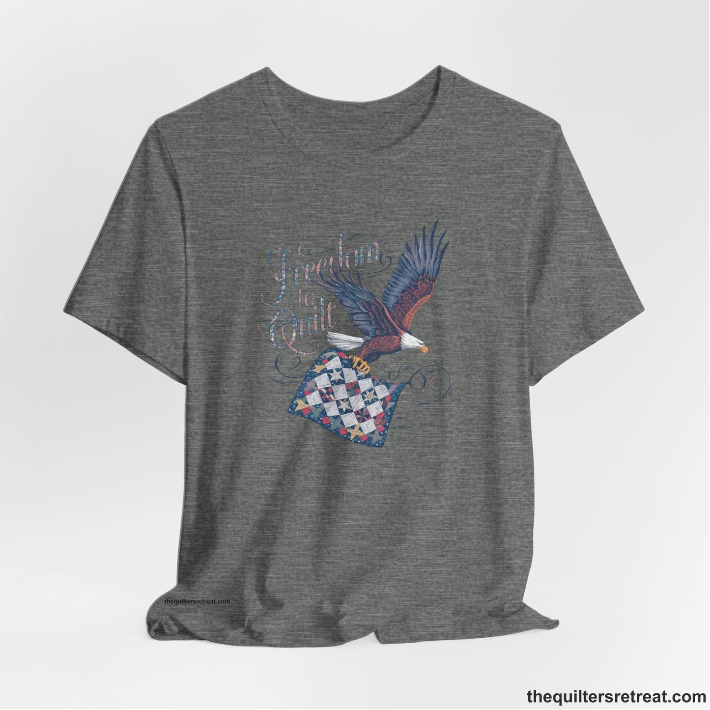 A Deep Heather Short Sleeve T-Shirt with a freedom to quilt text with an eagle carrying a colorful patchwork quilt in vintage style
