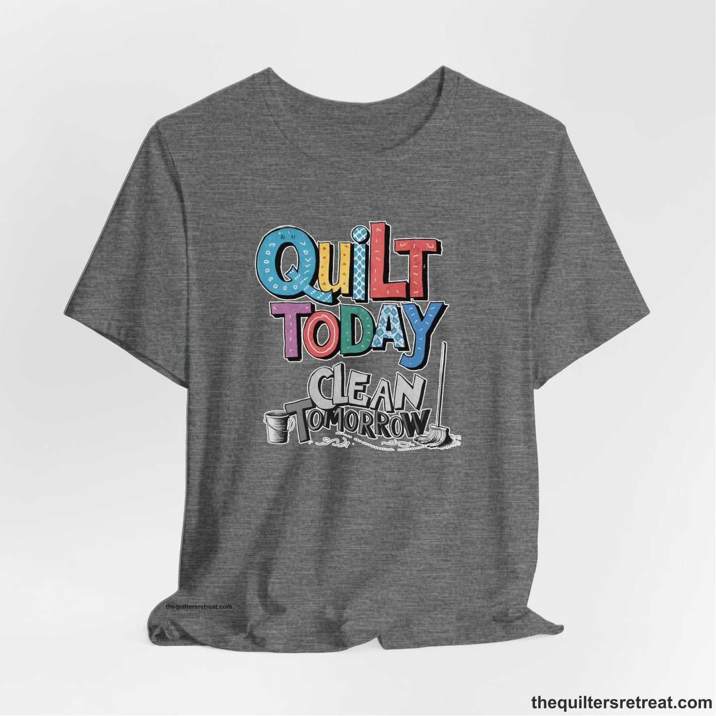 A Deep Heather Short Sleeve T-Shirt with a playful "Quilt Today Clean Tomorrow" text with colorful patterns and cleaning tools illustration