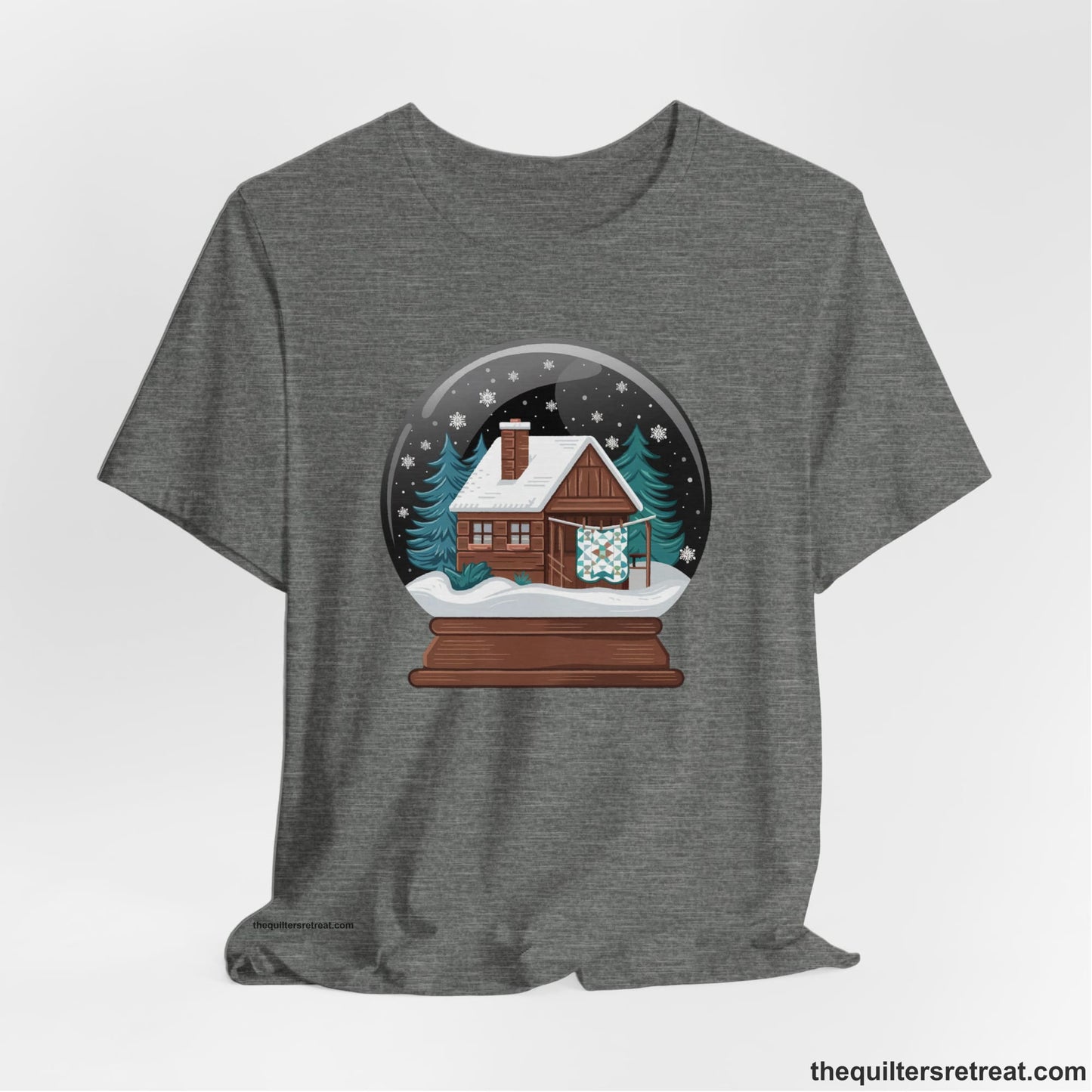 A Deep Heather Short Sleeve T-Shirt with a cabin in a snow globe with snowflakes and trees, in a cozy rustic style
