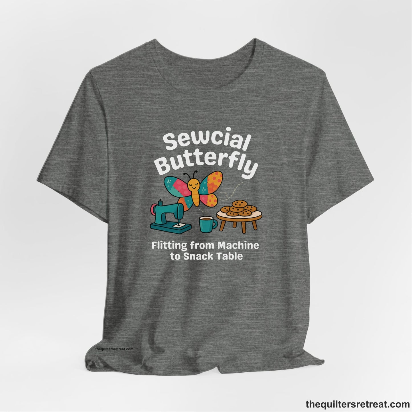 A Deep Heather Short Sleeve T-Shirt with a playful butterfly near sewing machine with cookies and coffee doodle design