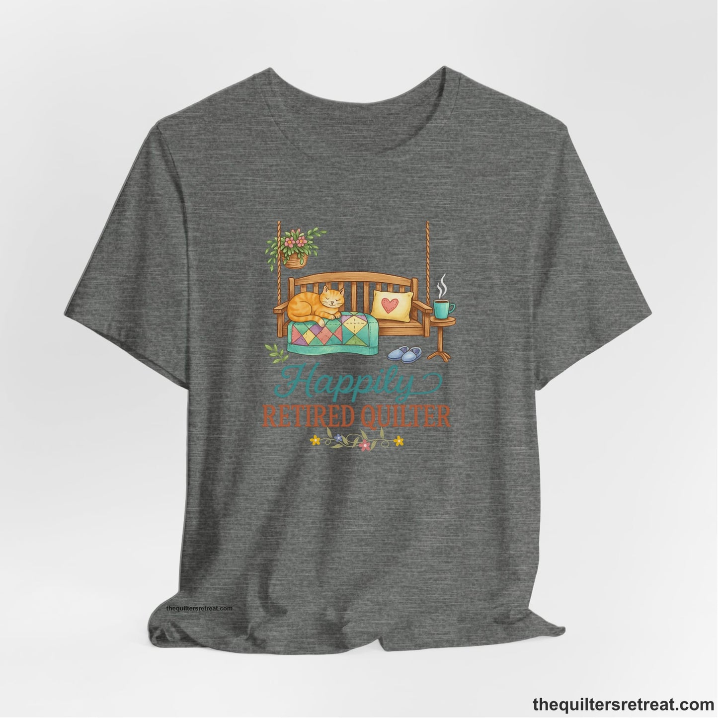 A Deep Heather Short Sleeve T-Shirt with a hanging bench with cozy cat and quilt, surrounded by plants, "Happily Retired Quilter" text