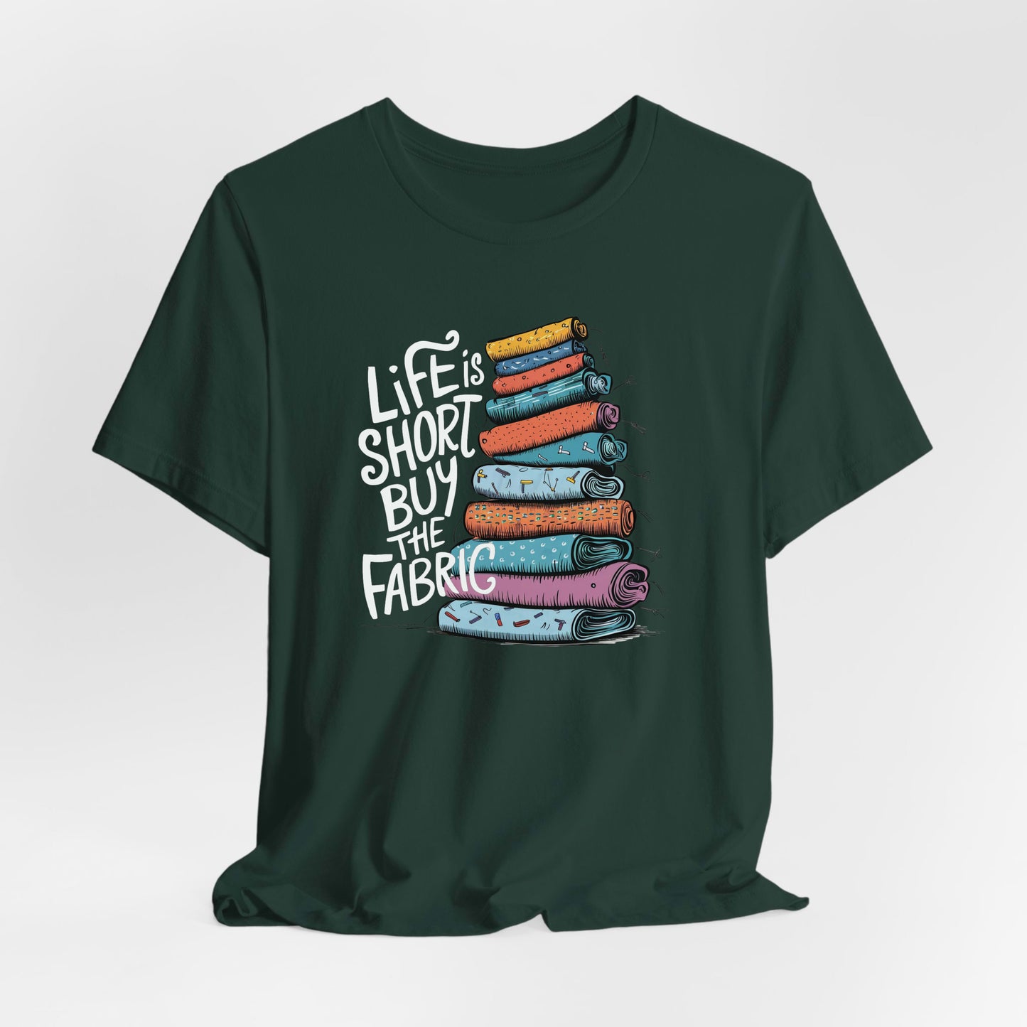A Forest Short Sleeve T-Shirt with a illustration of colorful fabric rolls with bold "Life is Short Buy the Fabric" text