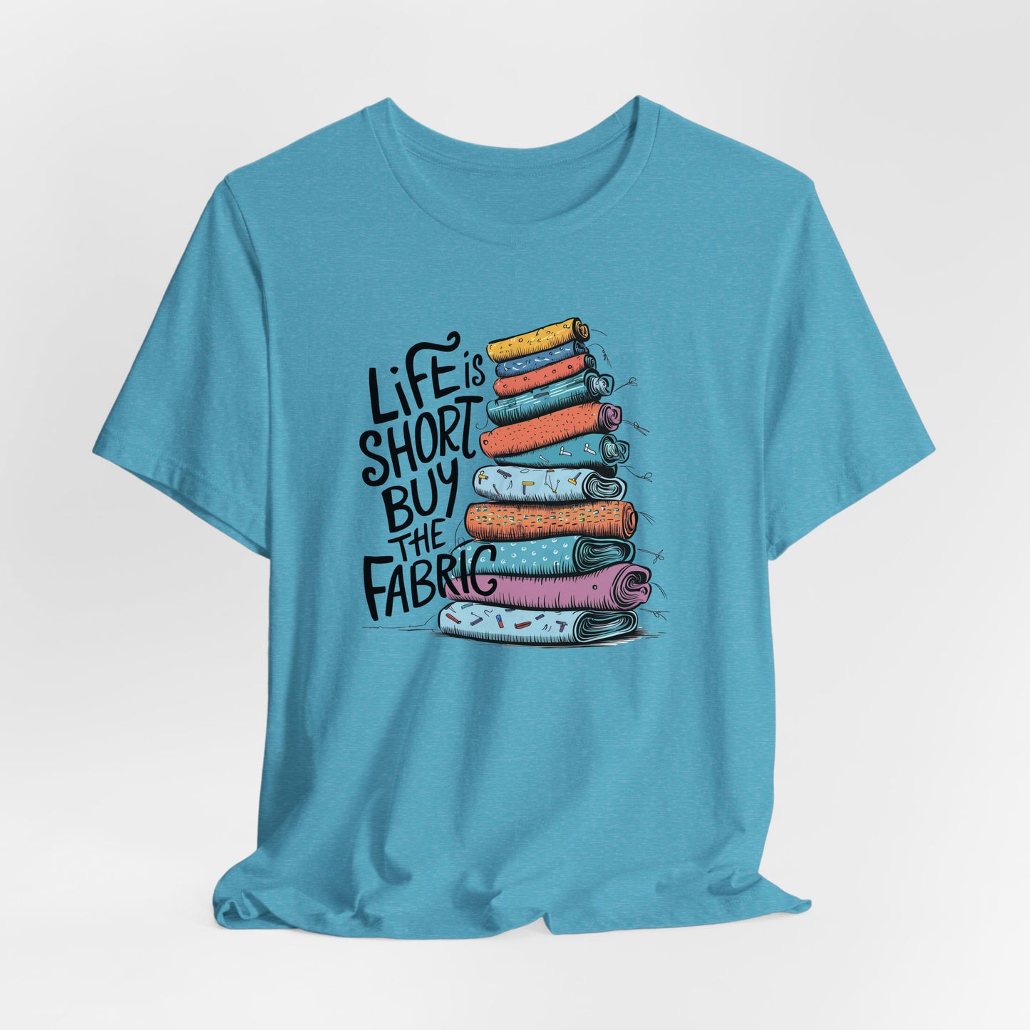 A Heather Aqua Short Sleeve T-Shirt with a illustration of colorful fabric rolls with bold "Life is Short Buy the Fabric" text